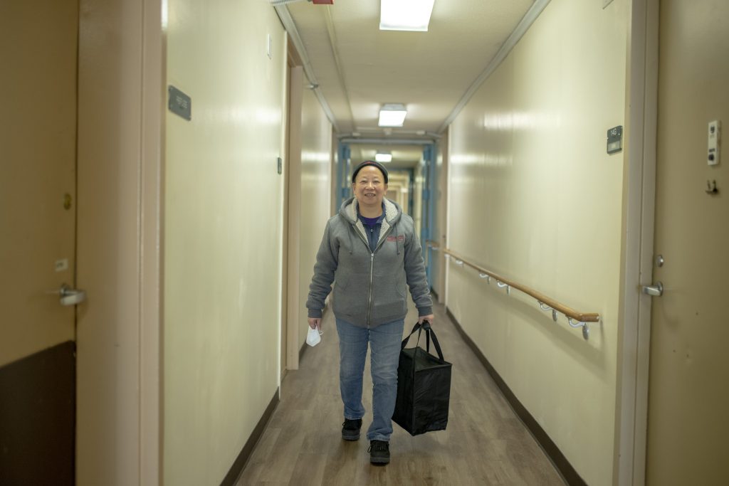 Mei Juan Zhao carries a meal delivery bag down the hallway of the Huangs' apartment building