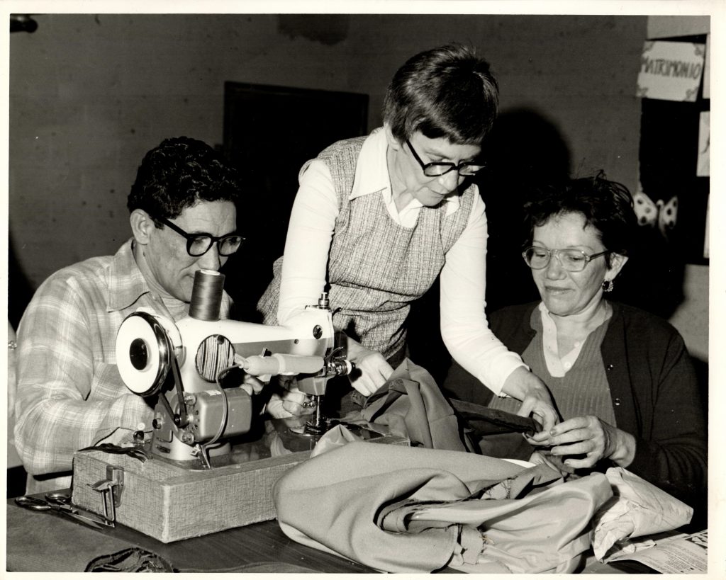 Ruth Taube helps two adult students at a sewing machine, circa 1970s