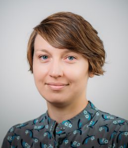 A woman with short brown hair in a gray top with a blue pattern.