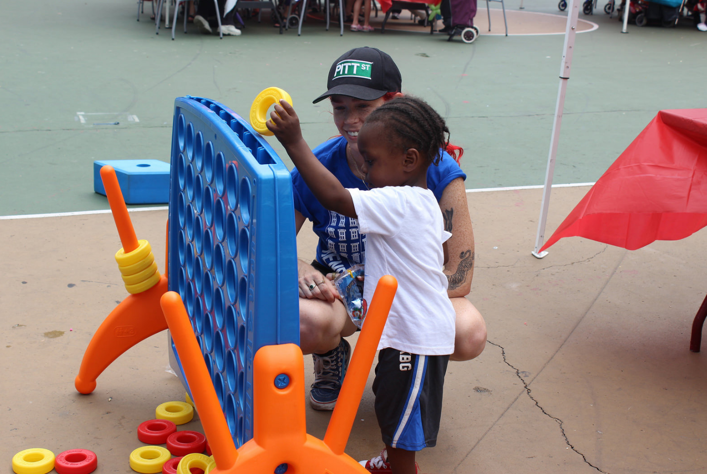 Volunteer helping child play Oversized COnnect Four outdoors at Community Day