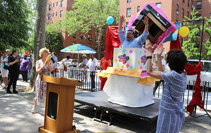 Henry Street president David Garza jumps out of a "cake" at street fair event, with people applauding