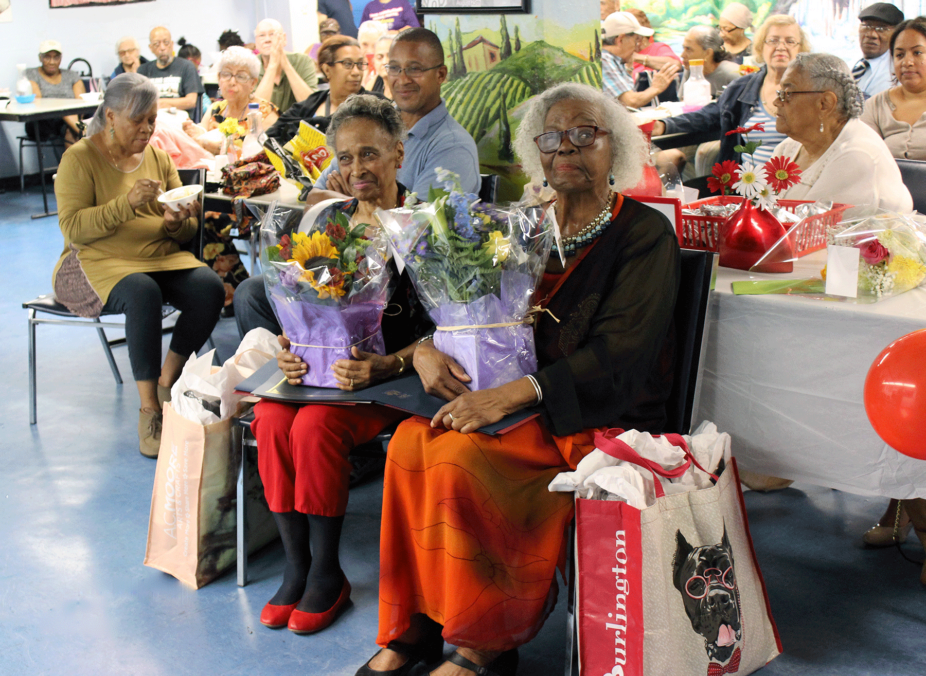 Two senior citizens being honored, sitting with flowers