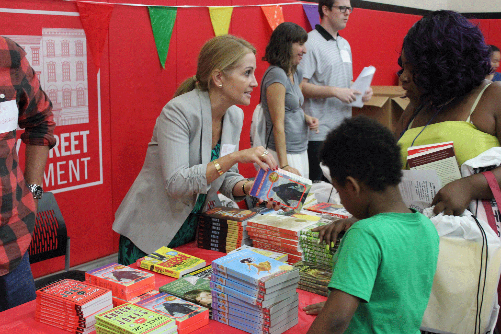 Volunteer gives mother and child a book at back to school event