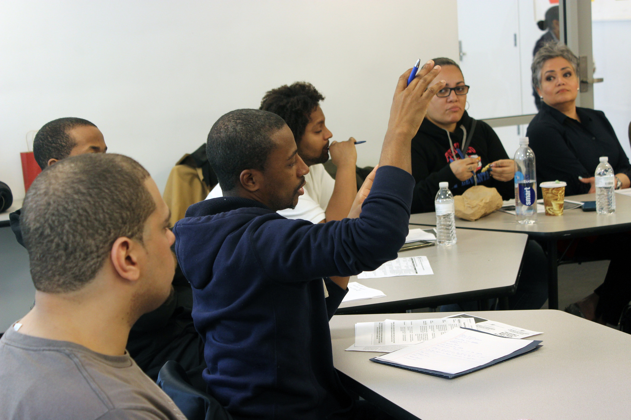 Adults in classroom setting, with one adult raising his hand