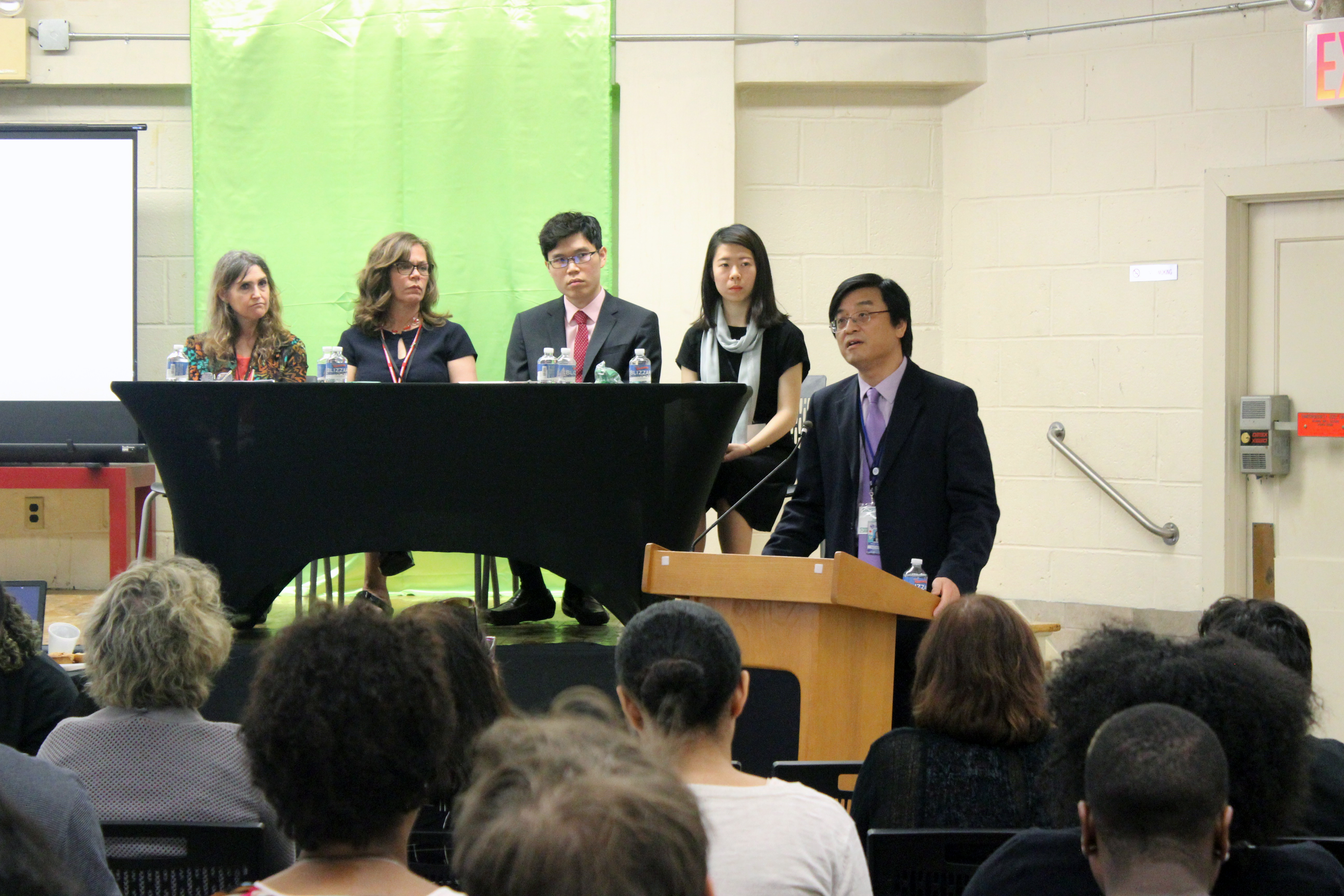 Panel and man at podium address audience