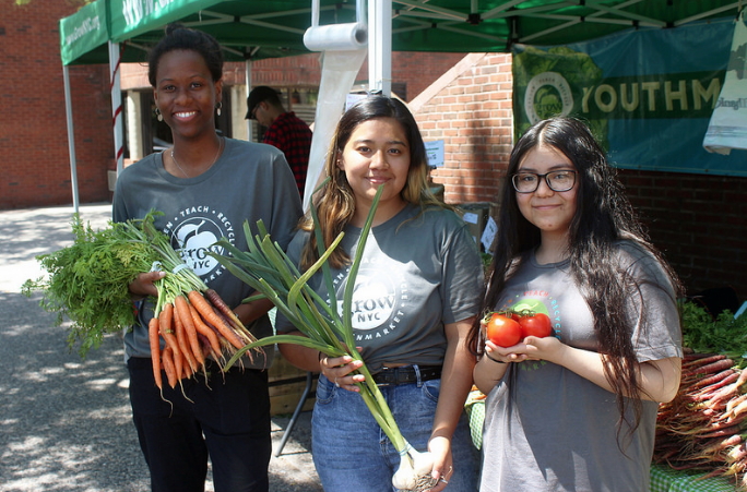 Youth employees of Greenmarket hold vegetables and smile for camera