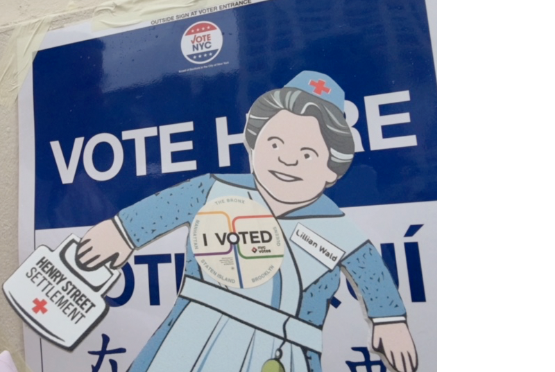 Flat Lillian, a paper doll representation of Henry Street Settlement founder Lillian Wald, outside of a polling location with 'I Voted' button