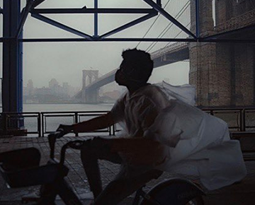 Person in a mask and poncho rides a bike under the Brooklyn Bridge