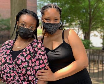 A Black woman poses with her daughter. They both wear black masks with their hair pulled back.