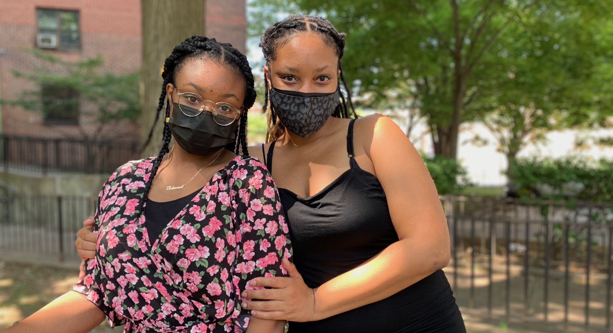 A Black woman poses with her daughter. They both wear black masks with their hair pulled back.