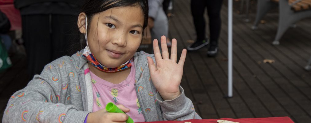 Young girl waves at camera while doing arts and crafts