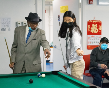 A teen volunteer plays pool with a member of the Henry Street Settlement Older Adult Center