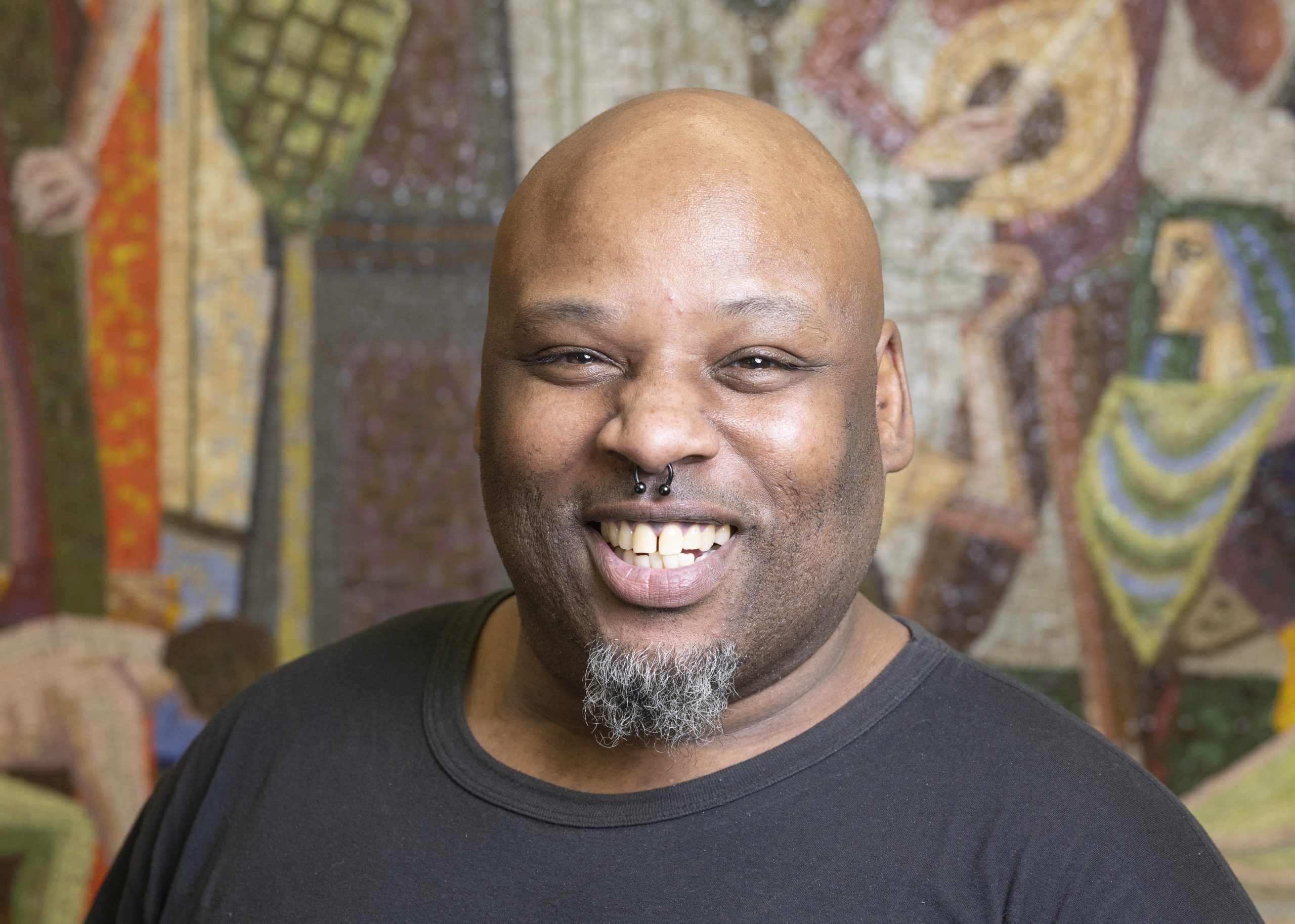 Korey Smith, a Black man with bald head and trimmed beard, smiles for a portrait in the Community Consultation Center community room
