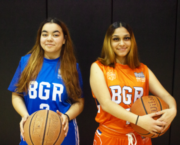 Two teen girls wearing uniforms and holding basketballs