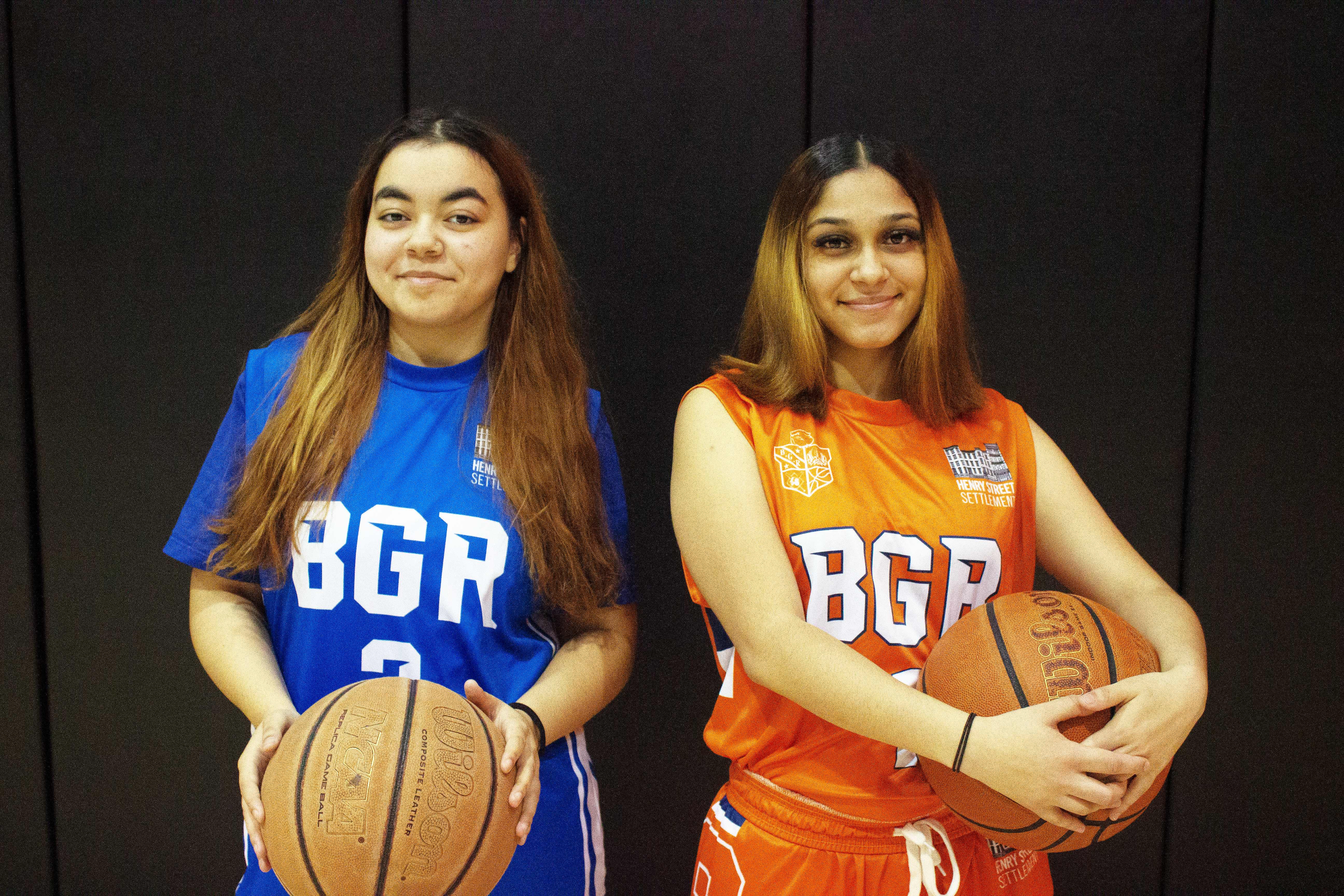 Two teen girls wearing uniforms and holding basketballs