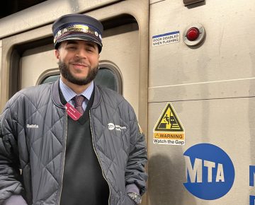 A man in a conductor's uniform stands in front of a Metro North train.