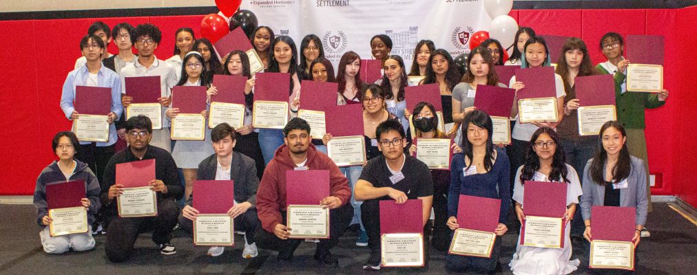 A large group of students pose together in rows, proudly holding certificates and folders during a graduation or recognition ceremony.